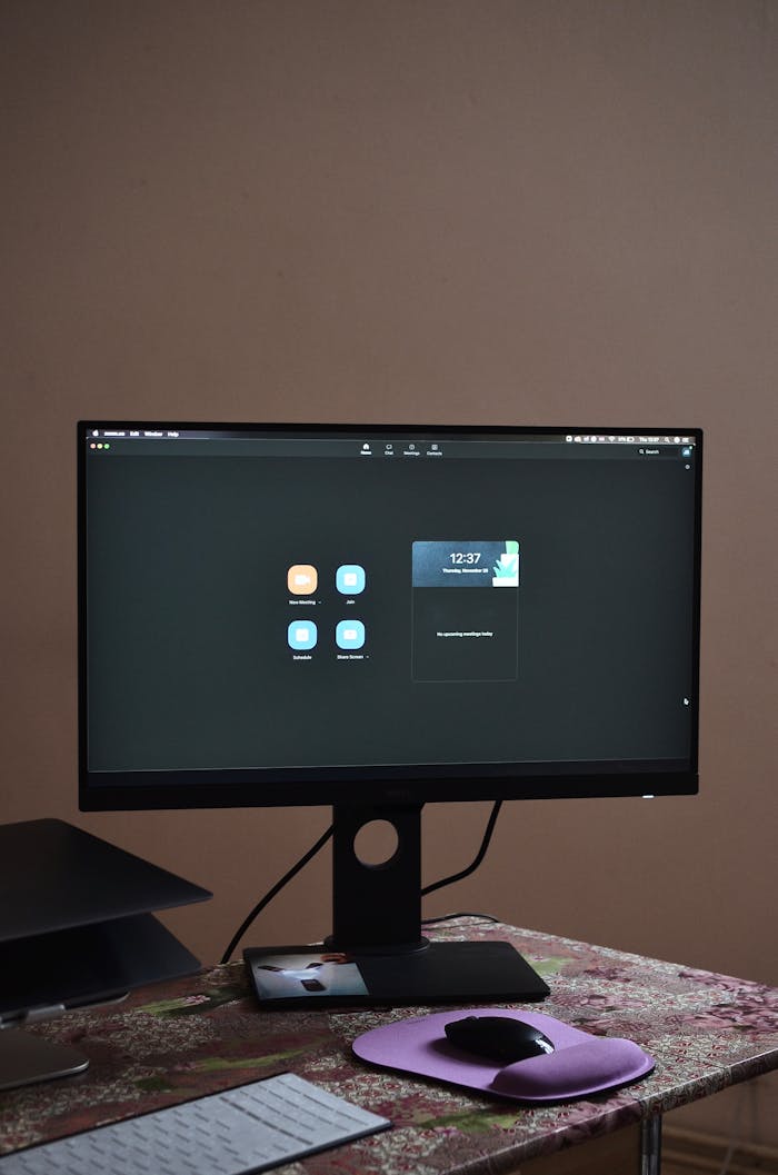 Contemporary stationary black monitor with white keyboard and mouse placed on desk against brown wall in room at convenient workplace